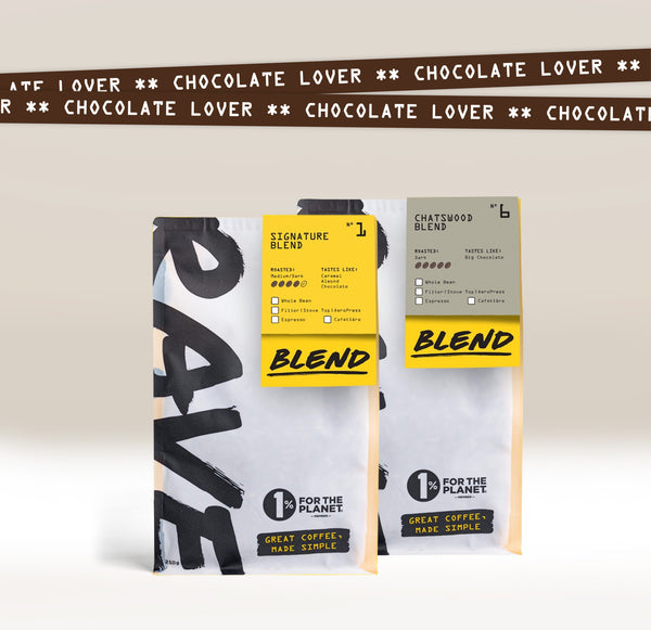 Two Ravecoffee bags, Signature Blend and Chatswood Blend, stand upright with yellow tags. A chocolate brown strip above reads "CHOCOLATE LOVER"—the perfect Chocolate Lover Coffee Bundle for fans of chocolate-flavored coffee.