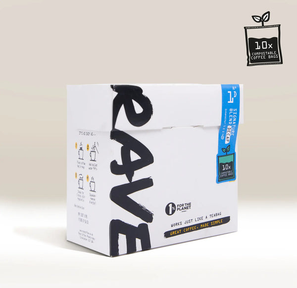 A white cardboard box of Rave Coffee by 1 for the Planet, featuring bold black brushstroke lettering and a blue vertical label, shown on a light beige background with a small product badge in the top right corner.