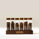 Six Coffee Bean Dosing Tubes filled with beans and topped with wooden lids, standing in a wooden coffee station organizer.