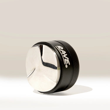 A metallic, round Rave 54mm Espresso Distributor from RAVE Coffee, featuring a shiny silver top and black side with the word “RAVE” in white, sits on a light surface casting a shadow.