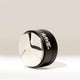 A metallic, round Rave 54mm Espresso Distributor from RAVE Coffee, featuring a shiny silver top and black side with the word “RAVE” in white, sits on a light surface casting a shadow.