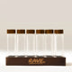 Six clear glass Coffee Bean Dosing Tubes (Set of 12) with dark wood lids standing in a matching wooden base.