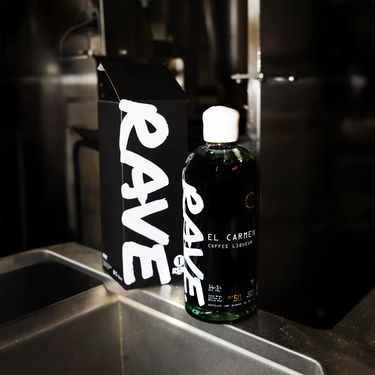 Bottle of Rave El Carmen Coffee Liqueur placed beside coffee equipment in a modern kitchen.