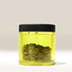 A well-lit, neutral background showcases the Comandante Polymer Bean Jar - Yellow by Comandante. The transparent jar with a black lid is half-filled with yellow liquid and whole coffee beans, ideal as a Comandante C40 accessory.