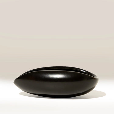 A glossy black ceramic bowl with a wide, rounded, boat-like shape, shown on a clean light beige background.