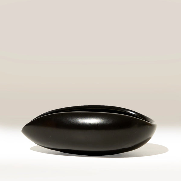 A glossy black ceramic bowl with a wide, rounded, boat-like shape, shown on a clean light beige background.