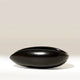 A glossy black ceramic bowl with a wide, rounded, boat-like shape, shown on a clean light beige background.