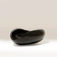 A glossy black curved bowl or dish with a smooth, rounded organic shape, photographed on a clean light gray studio background.