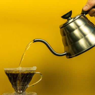 A photo of a person pouring coffee from a v60 dripper into a glass cup that has filter paper inside it.
