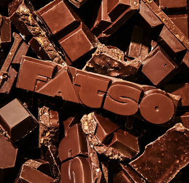 A pile of dark RAVE X FATSO Chocolate Bar pieces, with the word FATSO embossed across a central bar.