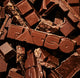 A pile of dark RAVE X FATSO Chocolate Bar pieces, with the word FATSO embossed across a central bar.