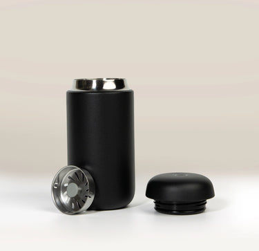 A matte black Fellow Carter Move Mug (12oz) with its lid removed and a metal splash guard standing next to it.