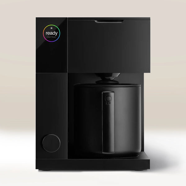 The Fellow Aiden Precision Drip Filter Coffee Maker by Fellow features a modern black design, a circular top-left display with colorful "ready" text, a large black carafe, customizable temperature controls, and an uncluttered light background.