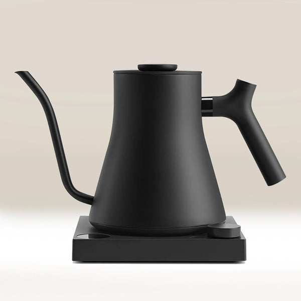 The Fellow Stagg EKG Pro Electric Kettle by Fellow, featuring a matte black finish, precision spout, and ergonomic handle, rests on its matching rectangular base against a neutral background.