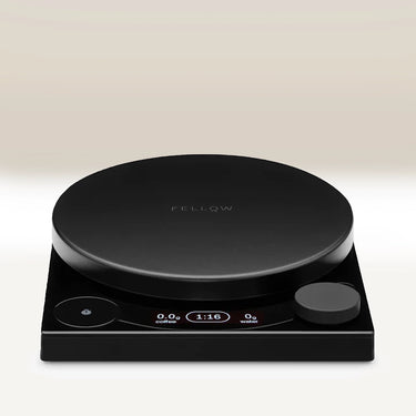 The Fellow Tally™ Pro Precision Scales by Fellow is a sleek black digital coffee scale with Brew Assist Mode, a round surface, display screen, and control knobs on a square base. It measures pour-over coffee weight, time, and water.