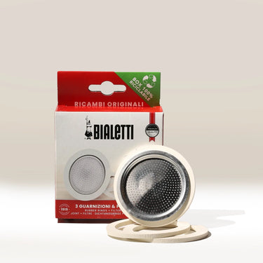 The Bialetti Gasket and Filter Plate for 3/4 Cup, shown in front of a red and white Bialetti box, includes a metal filter plate and two white gaskets.