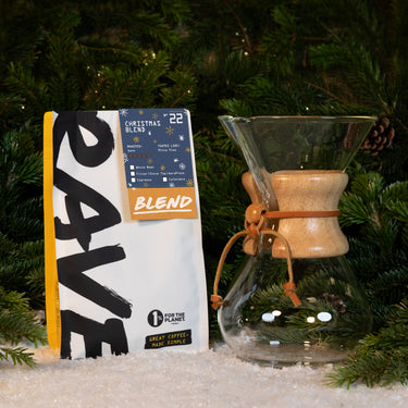 A Chemex Gift Set next to a bag of coffee beans in front of a Christmas tree with faux snow.