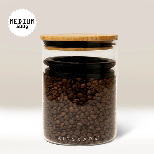 The Planetary Design Glass Airscape Coffee Storage Container, featuring a bamboo lid and Airscape technology, holds medium roast coffee beans. A label reading MEDIUM 500g in the top left corner highlights its effective oxygen removal for freshness.