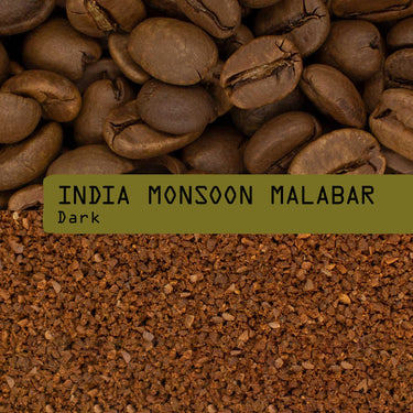 A close-up of coffee beans above coarsely ground Indian Monsoon Malabar Coffee Nº 53, with a green label in the center reading INDIA MONSOON MALABAR Dark in bold, typewriter-style font.