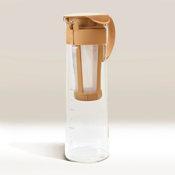 The Hario Cold Brew Coffee Pot by Hario is a clear glass pitcher with measurement markings, a beige lid, and an integrated filter for cold brew concentrate, displayed against a light neutral background.