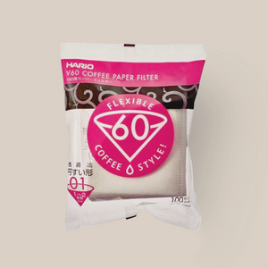A pack of 100 Hario Filter Papers V60 01 Dripper, featuring the brand's pink and white design and Japanese text. Cone-shaped disposable filters are visible inside the clear packaging. Suitable for use with Hario V60 01 drippers.