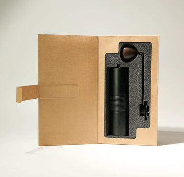 The AeroPress Gift Set with Grinder by Aeropress features a manual coffee grinder and metal handle in a custom foam insert, packaged in an upright box—ideal for use with your AeroPress coffee maker.