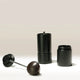 A black Hario Kabuto Coffee Grinder by Hario is shown disassembled on a neutral background, displaying the wooden-knob handle, cylindrical body with stainless steel burr, and detachable bottom container as its three main parts.