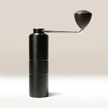 The Hario Kabuto Coffee Grinder by Hario is a black, entry-level grinder with a metal handle, dark wooden knob, textured grip, and durable stainless steel burr, shown standing upright on a light background.