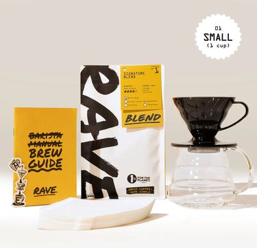 The Hario Hand Brewed Coffee Gift Set by Hario includes a RAVE Blend coffee bag, brew guide, paper filters, Hario V60 black pour-over dripper with glass carafe, and sticker—beautifully arranged on a neutral background.