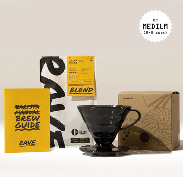 The Hario V60 Dripper Filter Coffee Gift Set by Hario includes freshly roasted coffee, a yellow brew guide booklet, a black plastic V60 dripper, and the brown V60 box, with a Medium (2-3 cups) label at the top right.