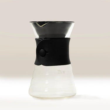 The Hario V60 Drip Decanter by Hario features a black silicone grip, wide spout, and curvy borosilicate glass base, showcasing a modern minimalist design on a neutral background.