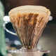 A close-up of the Hario V60 Clear Plastic Coffee Dripper Size 02 by Hario, featuring a paper filter with brewed coffee grounds and condensation on the clear dripper.