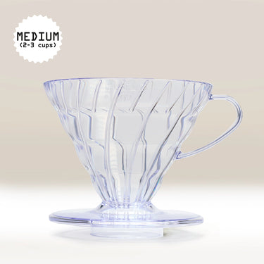 The Hario V60 Clear Plastic Coffee Dripper Size 02 by Hario, with vertical ridges and a handle, sits on a neutral background. Text in the top left reads “MEDIUM (2-3 cups),” highlighting its capacity for brewing multiple servings.