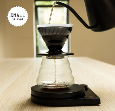 Coffee being poured into a glass coffee maker on a wooden surface.