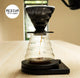 Coffee brewing apparatus with glass carafe and black pour-over on a wooden surface.
