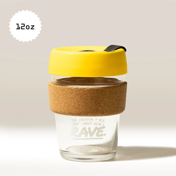 A 12oz KeepCup Rave Coffee Glass reusable cup with a cork band and yellow lid is set against a neutral background. The KeepCup brand name appears on the tempered glass.