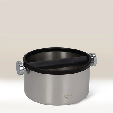 The MOTTA Knock Box 165mm features a sturdy stainless steel build with a black rubber bar for easy grounds disposal. The MOTTA logo appears on the front, set against a gradient beige background.