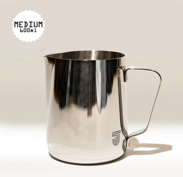 The Crema Pro Milk Steaming Jug, 20 OZ / 600ml, features a shiny stainless steel design with handle and small logo near the base. Perfect for latte art, it sits on a neutral background with 