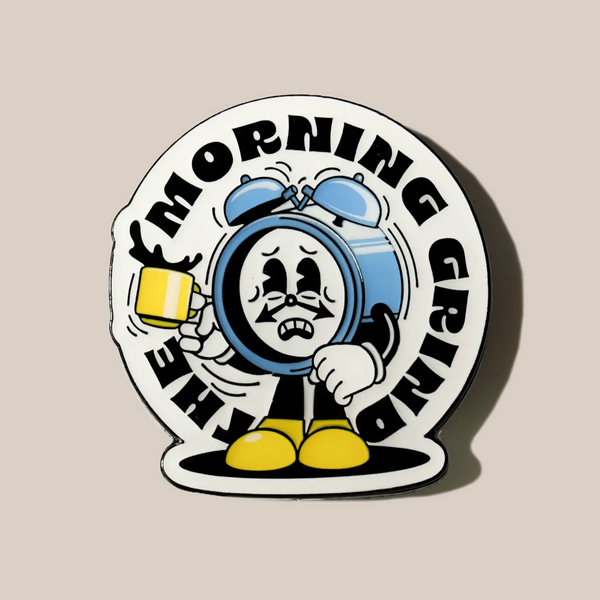 The RAVE Coffee Morning Grind Pin Badge features a tired cartoon alarm clock with yellow shoes, holding a yellow coffee mug. "THE MORNING GRIND" appears in playful retro text on a beige background—perfect for coffee lovers.