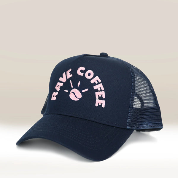 The RAVE COFFEE Navy Trucker Cap features a navy mesh design, pink embroidered RAVE COFFEE and coffee bean logo on the front, curved brim, and snapback closure—ideal for fans of classic trucker caps.