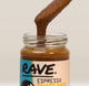 A close-up of a glass jar filled with Rave Espresso Salted Date spread, with a spoon lifting a thick, brown, textured paste above the rim. The label features the brand 'RAVE' and the flavor 'ESPRESSO SALTED DATE'.
