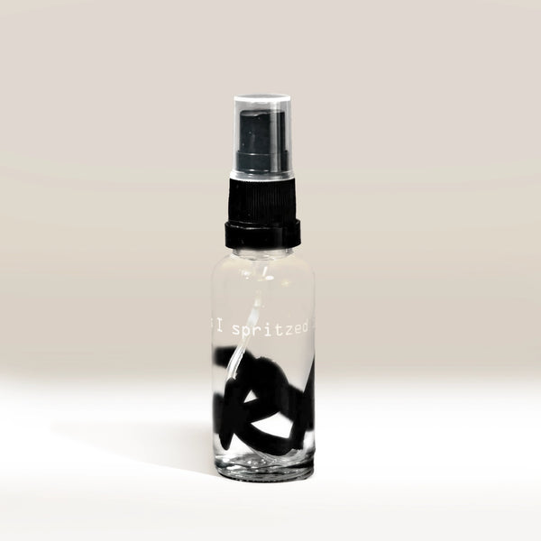 The RDT Bottle (Oops I Spritzed it Again) is a clear glass spray bottle with a black pump and quirky "I spritzed" text—ideal for coffee lovers. It rests on a softly lit, plain background, casting a subtle shadow.