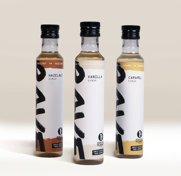 RAVE COFFEE Best Selling Syrup Set featuring three glass bottles of flavored coffee syrups labeled hazelnut, vanilla, and caramel.