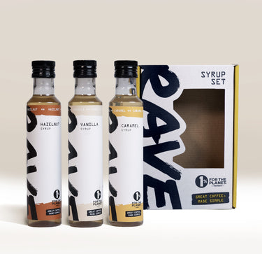 Three bottles of hazelnut, vanilla, and caramel RAVE COFFEE Best Selling Syrup Set standing in front of their rectangular cardboard gift box.
