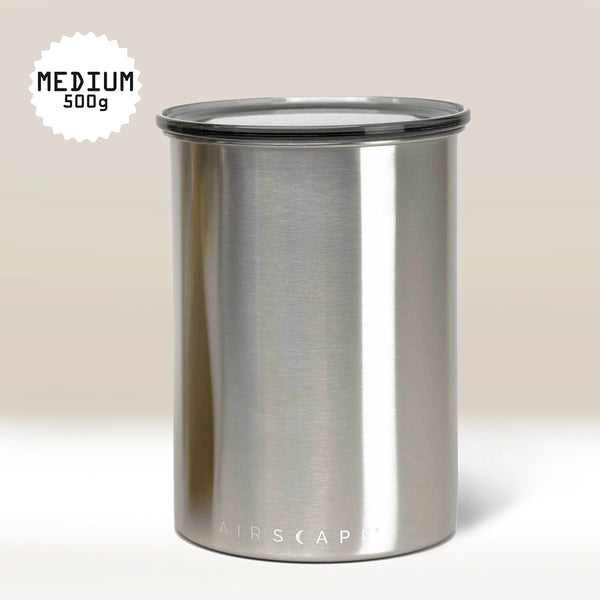 The Planetary Design Stainless Steel Airscape Coffee Storage Container features a black AIRSCAPE lid and a MEDIUM 500g label in the top left. Ideal for coffee, it sits against a soft beige gradient background.
