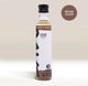 A bottle of Rave Coffee Syrups by RAVE COFFEE, featuring a black cap and labeled with BROWN SUGAR SYRUP and 1% for the Planet, sits against a beige background. A starburst graphic in the top right corner reads BROWN SUGAR, highlighting this UK-made flavoured coffee syrup.