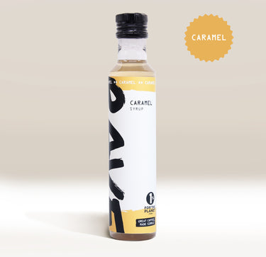 An upright bottle of Rave Coffee Syrups by RAVE COFFEE with a modern white and yellow label sits on a light background. A caramel-colored badge marked CARAMEL appears in the top right corner. Perfect for coffee syrup lovers.
