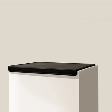The RAVE COFFEE Black Tamp Mat, featuring a white rectangular pedestal and a black silicone flat top, is showcased against a plain beige background—ideal for use as an espresso tamp mat.