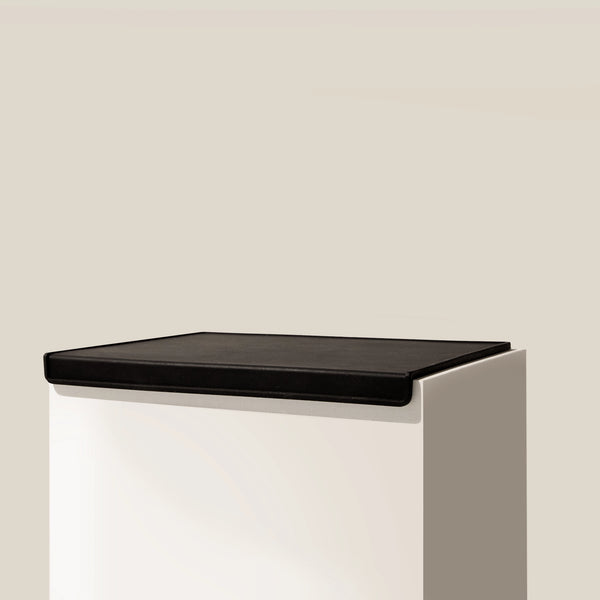 The RAVE COFFEE Black Tamp Mat, featuring a white rectangular pedestal and a black silicone flat top, is showcased against a plain beige background—ideal for use as an espresso tamp mat.