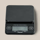 The Tiamo Timer Scale is a black coffee scale with a flat platform, built-in timer, “Start/Stop” and “On/Off/Tare” buttons, and a display for time and weight. The Tiamo brand name appears below the screen.
